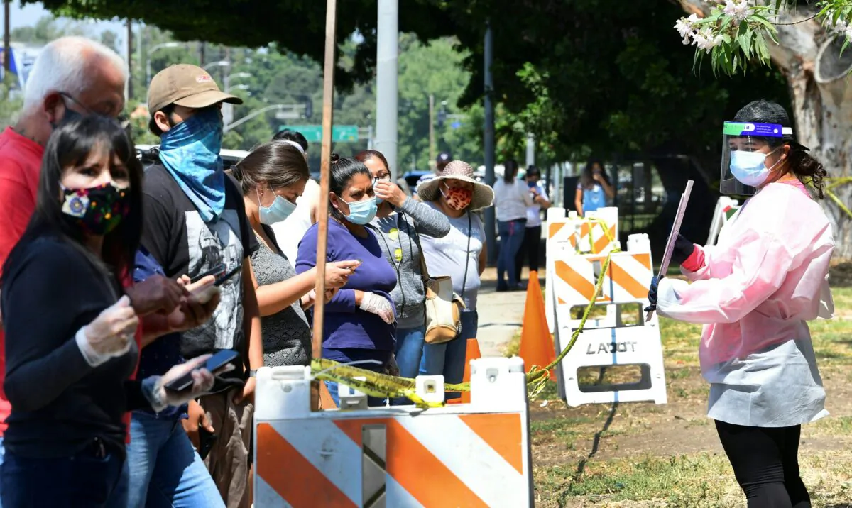 A volunteer dressed in personal protective gear offers instructions to people waiting in line at a walk-in COVID-19 test in Los Angeles, Calif., on July 17, 2020. (Frederic J. Brown /AFP via Getty Images)