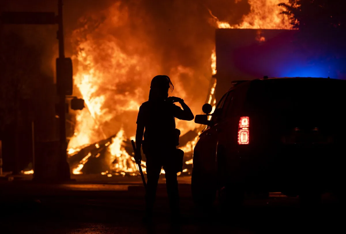 A police officer stands watch as a looted pawn shop burns behind them, in Minneapolis, Minn., on May 28, 2020. (Stephen Maturen/Getty Images)
