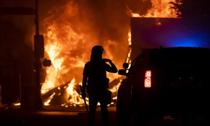 A police officer stands watch as a looted pawn shop burns in the background, in Minneapolis, Minn., on May 28, 2020. (Stephen Maturen/Getty Images)