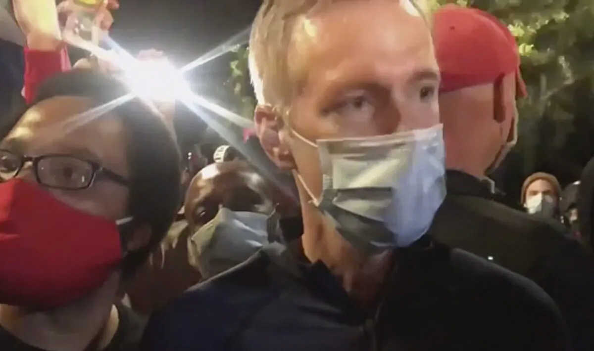 Portland Mayor Ted Wheeler (R) stands at a fence guarding a federal courthouse as tear gas drifts by, in Portland Ore., on July 23, 2020. (Karina Brown via AP)