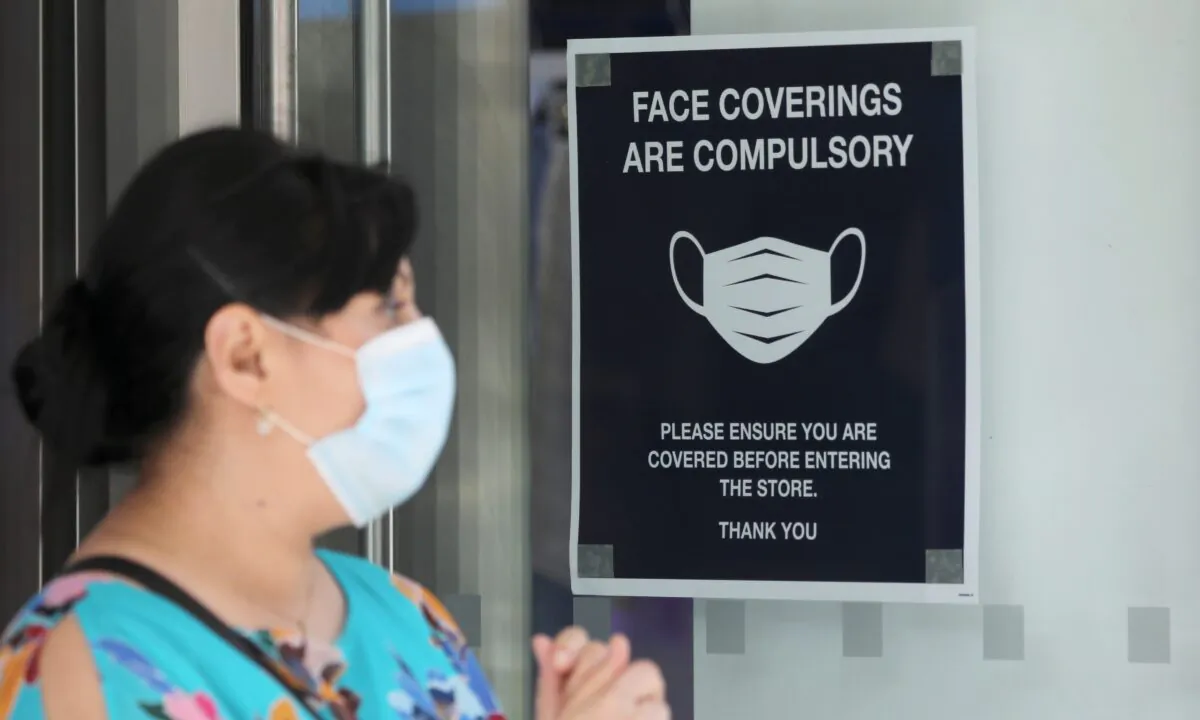 A woman wears a protective mask next to a sign urging to wear face coverings at a store, as the spread of the CCP virus continues, in London, Britain, on July 24, 2020. (Simon Dawson/Reuters)