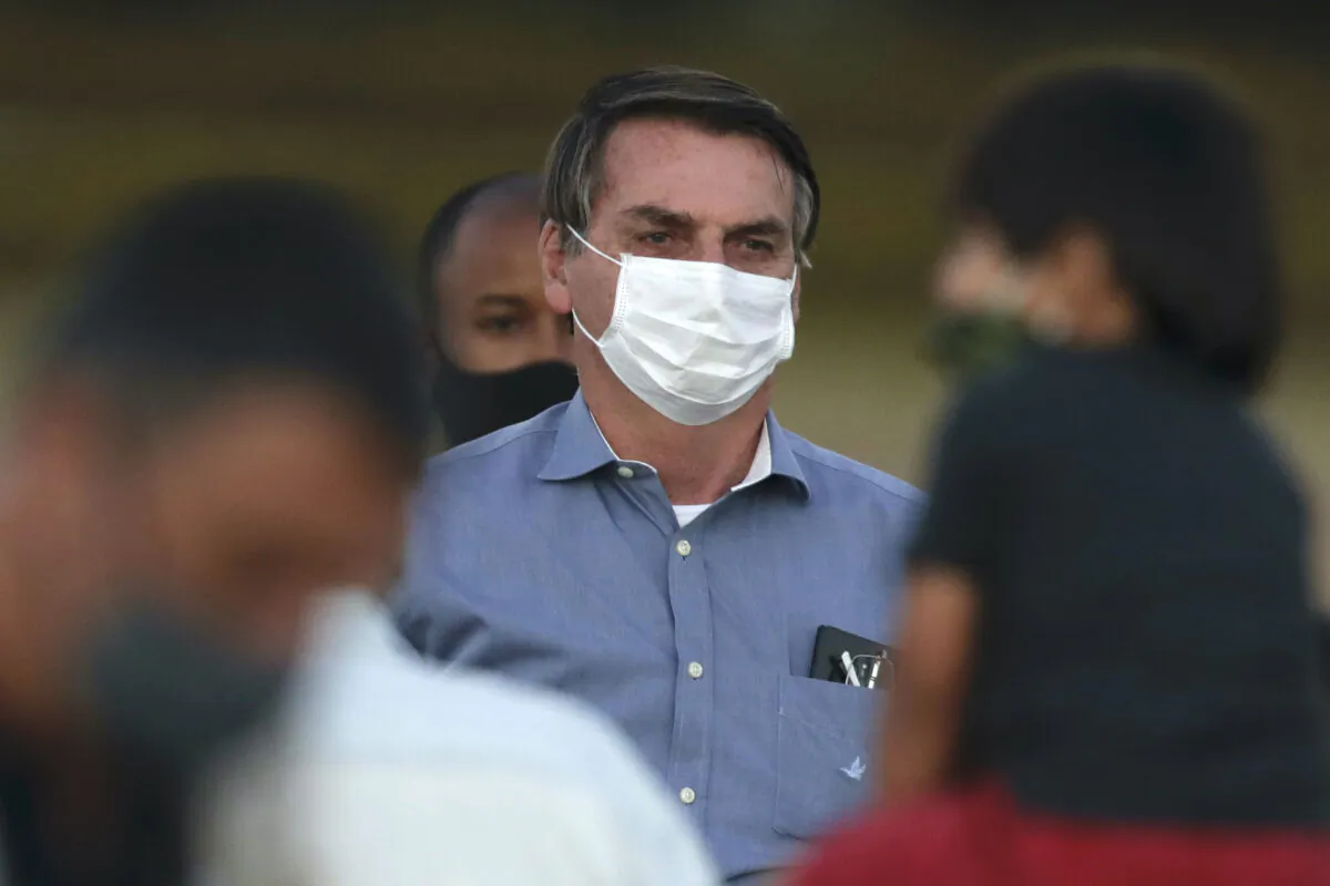 Brazil's President Jair Bolsonaro, who was infected with COVID-19, wears a protective face mask as he stands with supporters during a Brazilian flag retreat ceremony outside his official residence the Alvorada Palace, in Brasilia, Brazil, Fri., July 24, 2020. (Eraldo Peres/AP Photo)