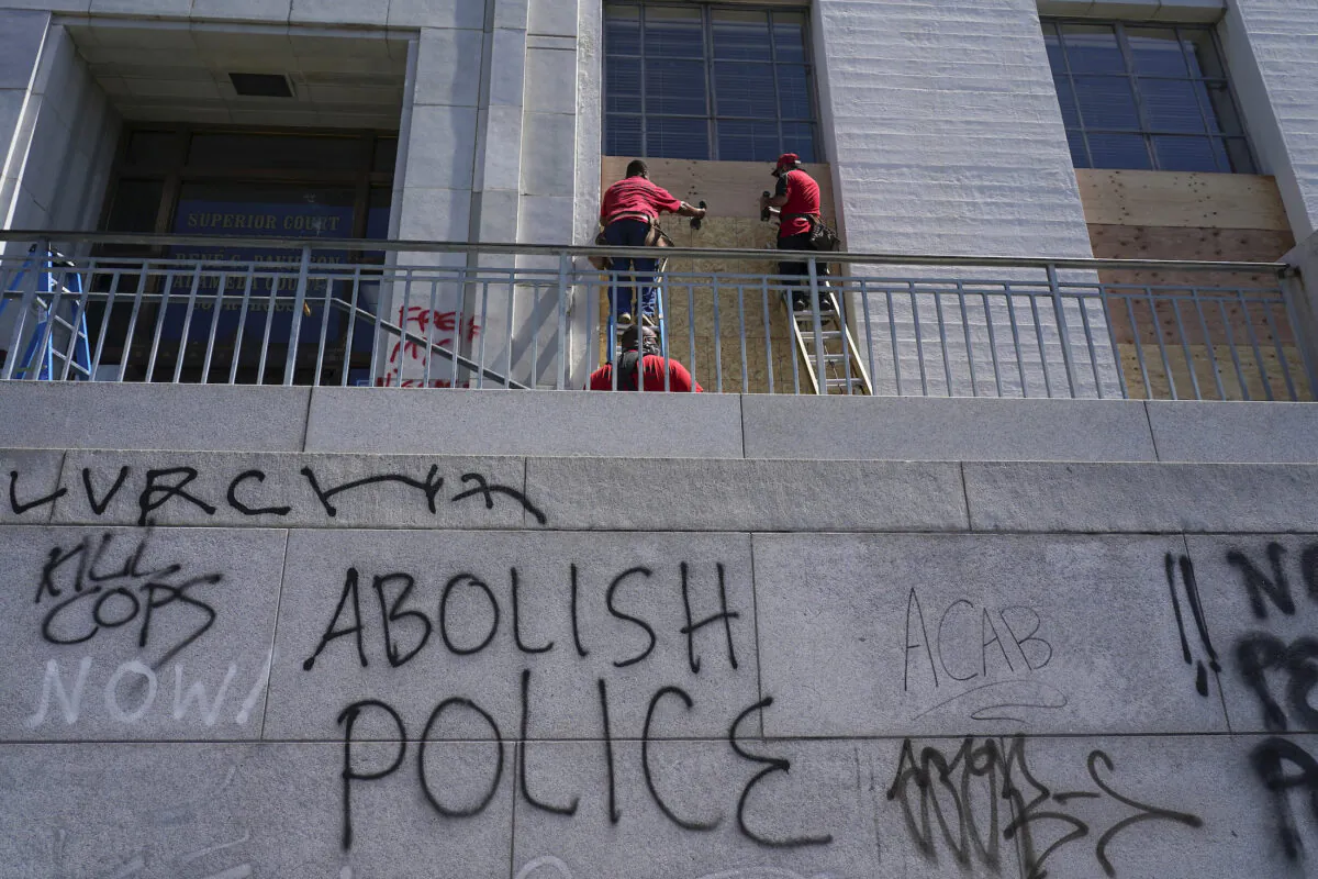 Workers place wooden boards over windows as graffiti is shown on walls at the Alameda County Courthouse in Oakland, Calif., on July 26, 2020. (Jeff Chiu/AP Photo)