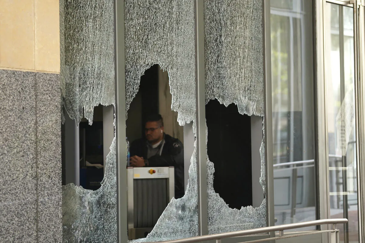 A man sits behind a broken glass from a window at the Ronald V. Dellums Federal Building in Oakland, Calif., on July 26, 2020. (Jeff Chiu/AP Photo)