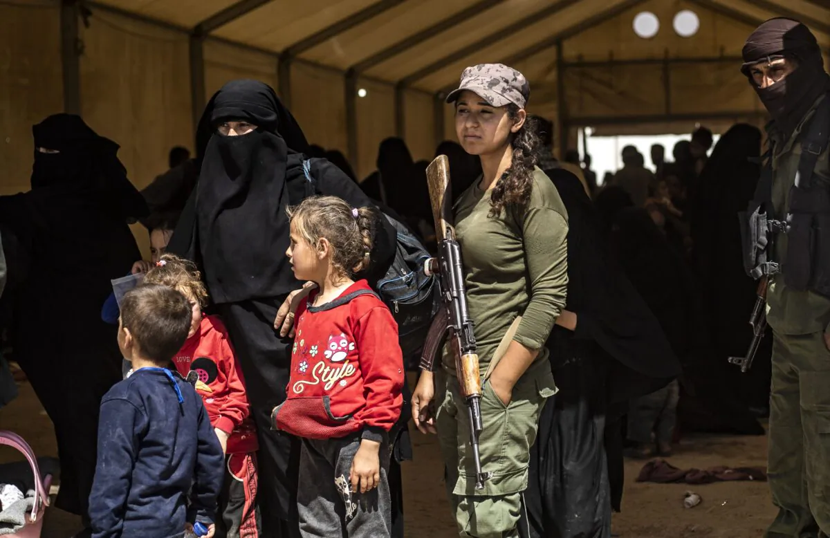Fighters from the Syrian Democratic Forces (SDF) stand guard as displaced people prepare to board a bus waiting outside the Al-Hol camp in northeastern Syria's Al-Hasakeh governorate on June 3, 2019, as Kurdish authorities started sending home 800 Syrian women and children who had been evacuated from the Islamic State group's "caliphate" earlier this year. (Delil Souleiman/AFP via Getty Images)