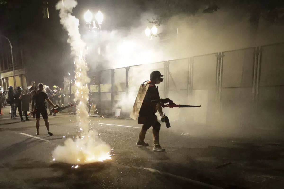 Demonstrators walk along a steel fence as federal officers launch tear gas during a riot outside the Mark O. Hatfield Courthouse in Portland, Ore., on July 26, 2020. (Marcio Jose Sanchez/AP Photo)