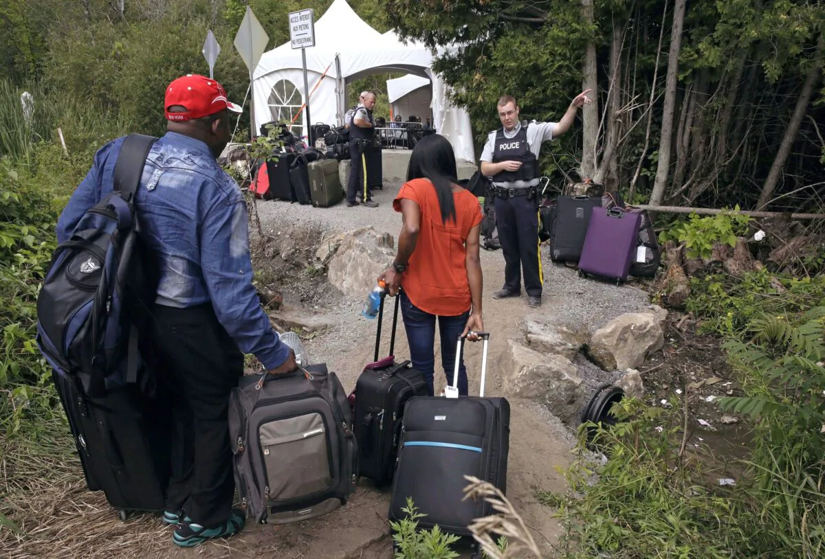 An RCMP officer informs a migrant couple of the location of an official border station, shortly before they illegally crossed from New York to Quebec via Roxham Road, on Aug. 7, 2017. (AP Photo/Charles Krupa, File)