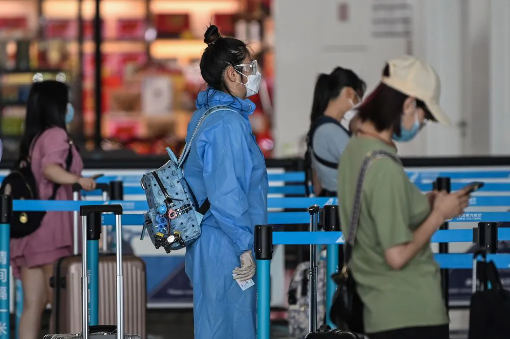 A passenger wearing protective gear and a mask waits in line at an airline counter at Tianhe airport in Wuhan, in central China's Hubei Province, on May 23, 2020. (Hector Retamal/AFP via Getty Images)