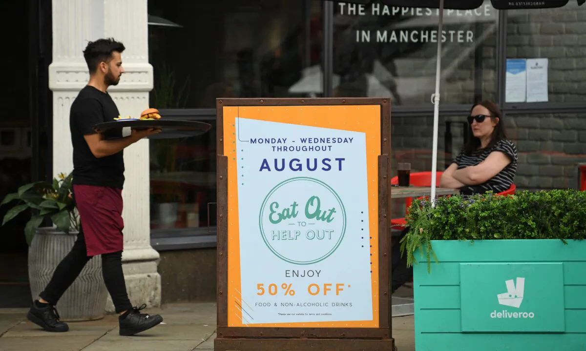 A server carries food past a sign promoting the British Government's "Eat Out to Help Out" scheme to get consumers spending again, outside a restaurant in Manchester, northwest England, on Aug. 3, 2020. (Oli Scarff/AFP via Getty Images)
