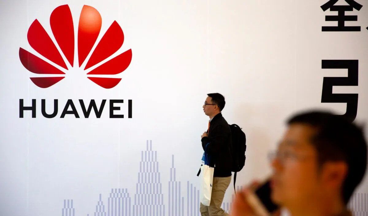 Man uses his smartphone as he stands near a billboard for Chinese technology firm Huawei at the PT Expo in Beijing on Oct. 31, 2019. (Mark Schiefelbein/AP Photo)