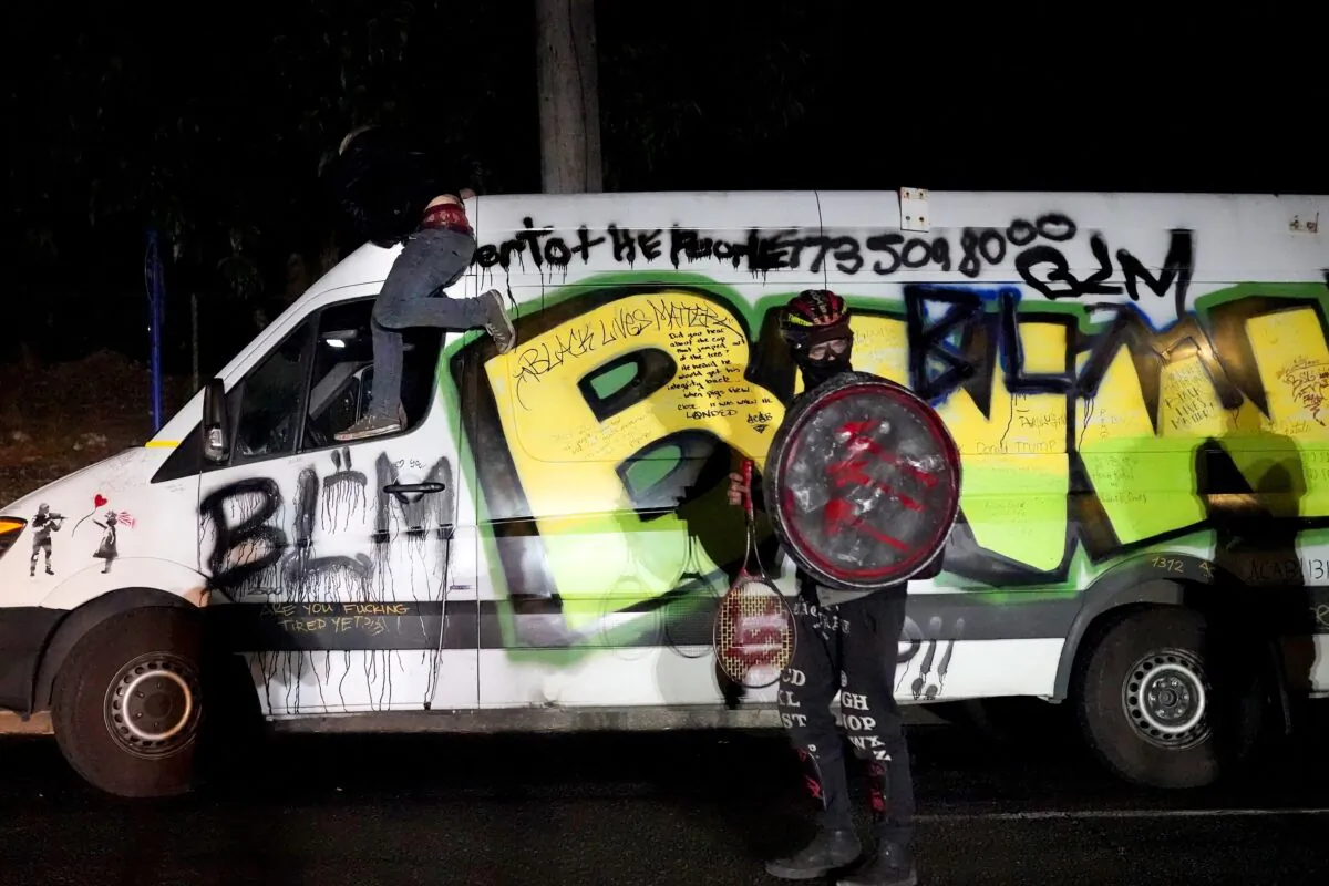 A man carrying a shield with a symbol linked to Antifa stands next to a van with Black Lives Matter imagery during a demonstration outside a Multnomah County sheriff's office building in north Portland, Ore., on Aug. 12, 2020. (Nathan Howard/Getty Images)