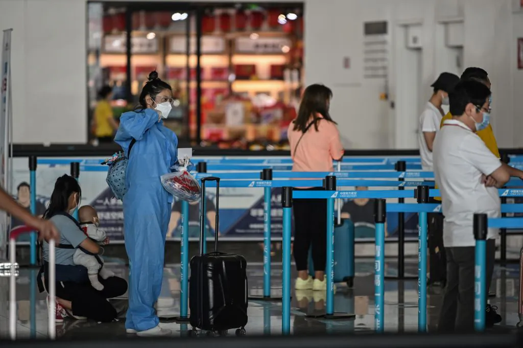 A passenger wearing protective gear and a mask waits in line at an airline counter at Tianhe airport in Wuhan, in central China's Hubei Province, on May 23, 2020. (Hector Retamal/AFP via Getty Images)