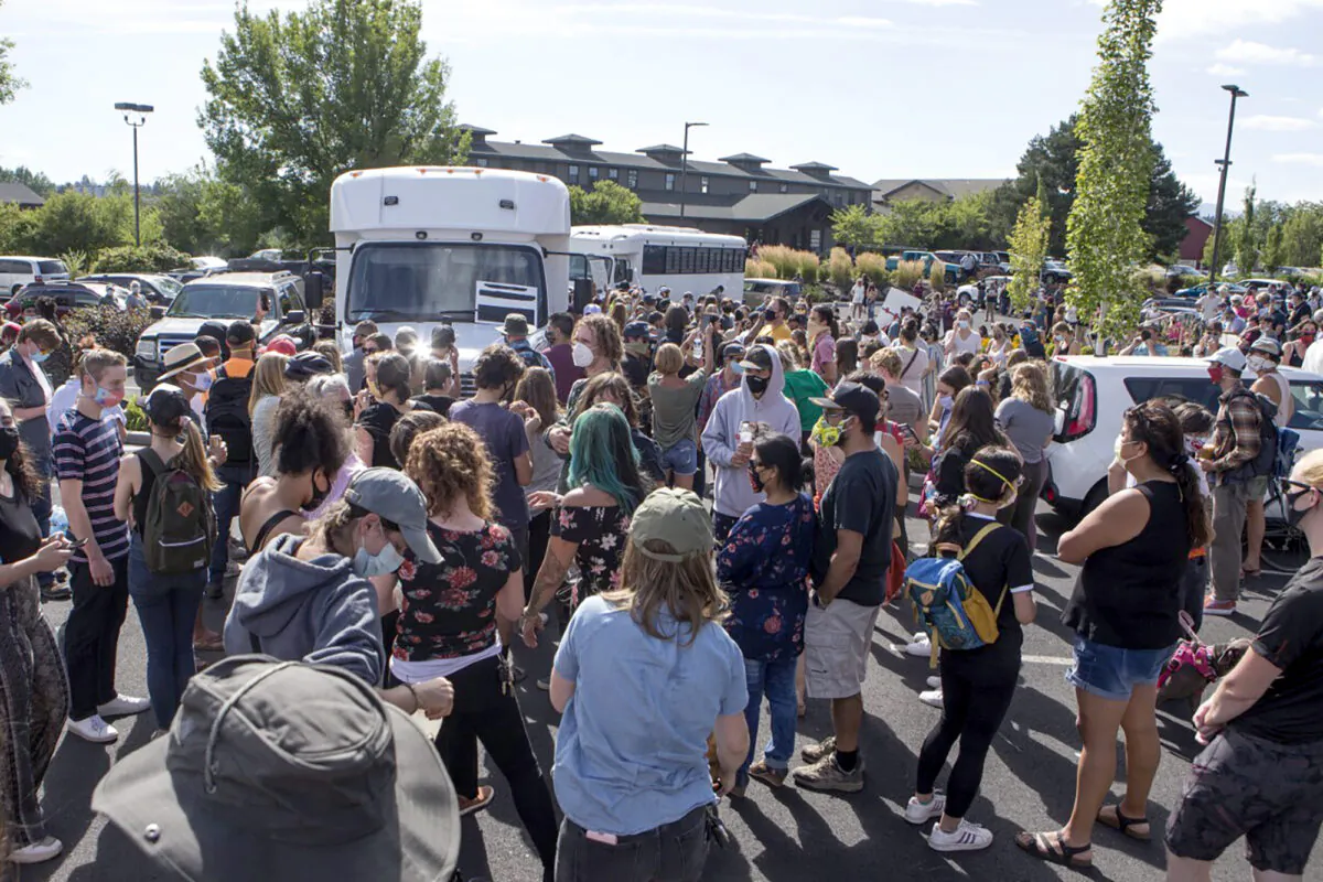 Hundreds of activists gather around two  buses outside the Crane Shed Commons in Bend, Ore., on Aug. 12, 2020. (Ryan Brennecke/The Bulletin via AP)