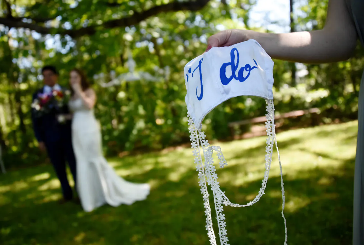 A bridesmaid holds on to the bride's face mask while newlyweds pose for pictures following their wedding ceremony in Rustburg, Va., on May 9, 2020. (Olivier Douliery/AFP/Getty Images)