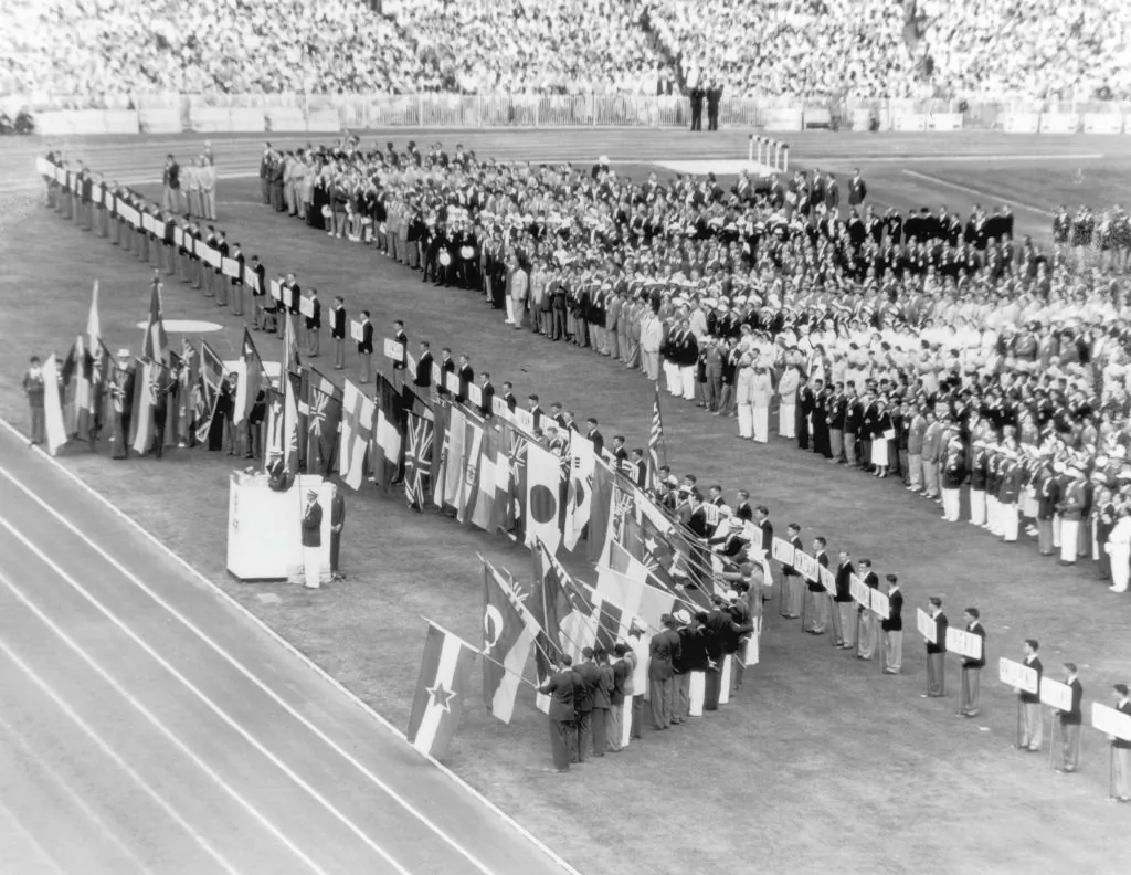 Australian athlete John Landy stands at the podium and takes the Olympic oath while athletes from competing nations hold their national flags during opening ceremonies for the Olympics, Melbourne, Australia, 26th November 1956. (Keystone/Hulton Archive/Getty Images)