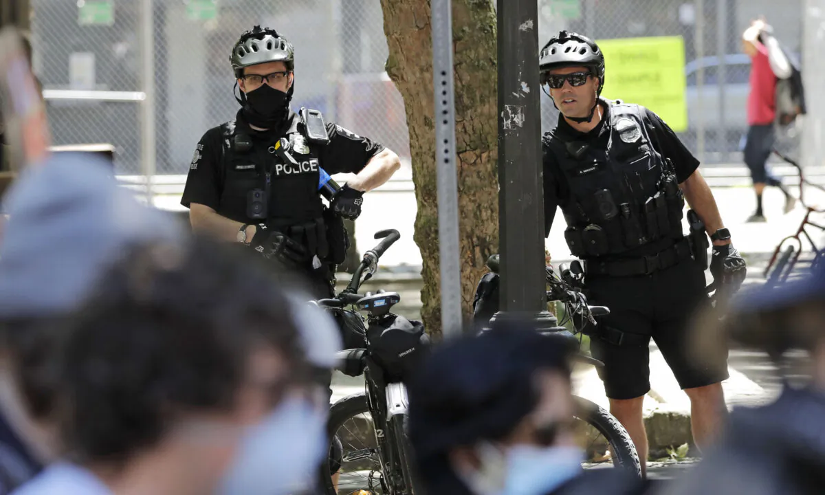 In this July 20, 2020, file photo, police officers look on at protesters in Seattle. (Elaine Thompson/AP Photo)