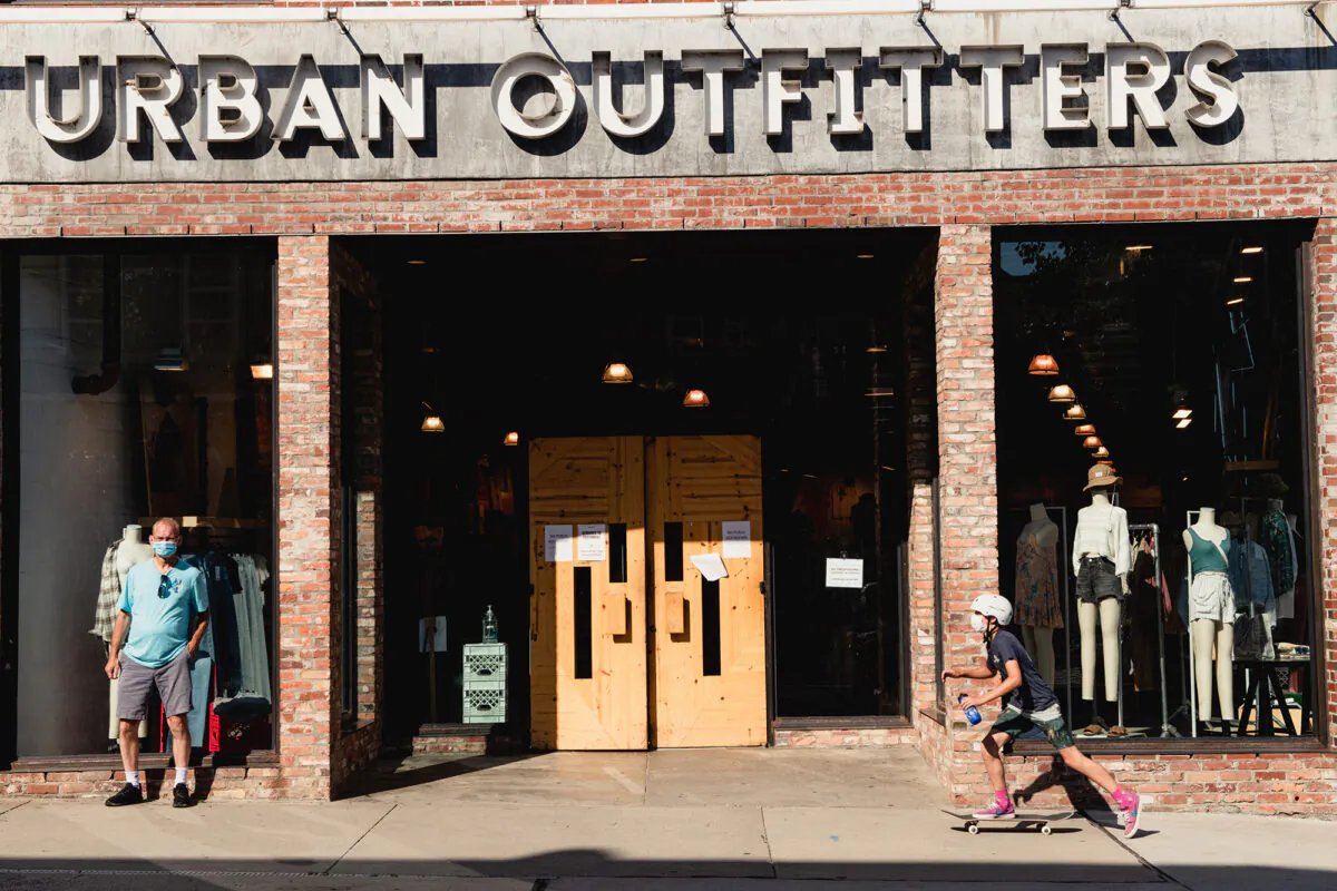 A person wearing a protective mask rides a skateboard past an Urban Outfitters store in downtown Asheville, N.C., on Wed., July 15 2020. (George Etheredge/Bloomberg via Getty Images )
