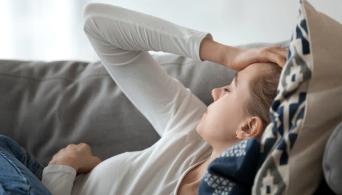 A woman holds her head as she lies on pillows. (Illustration - fizkes/Shutterstock)   