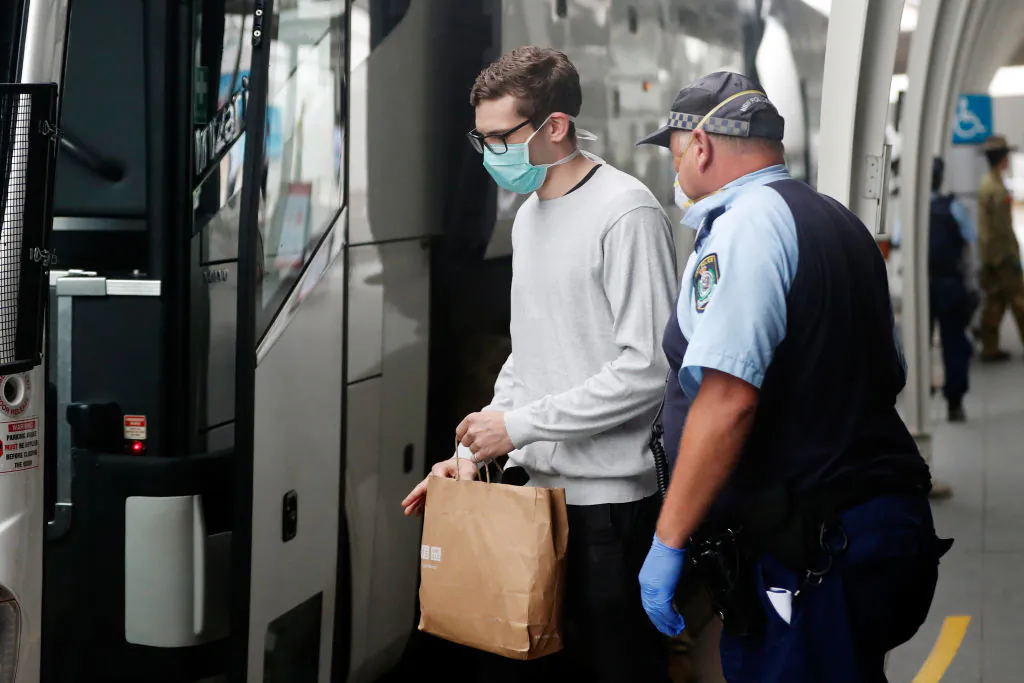 A member of the NSW Police Force escorts a returning overseas travellers onto waiting buses at Sydney Airport on March 30, 2020 in Sydney, Australia. (Brendon Thorne/Getty Images)
