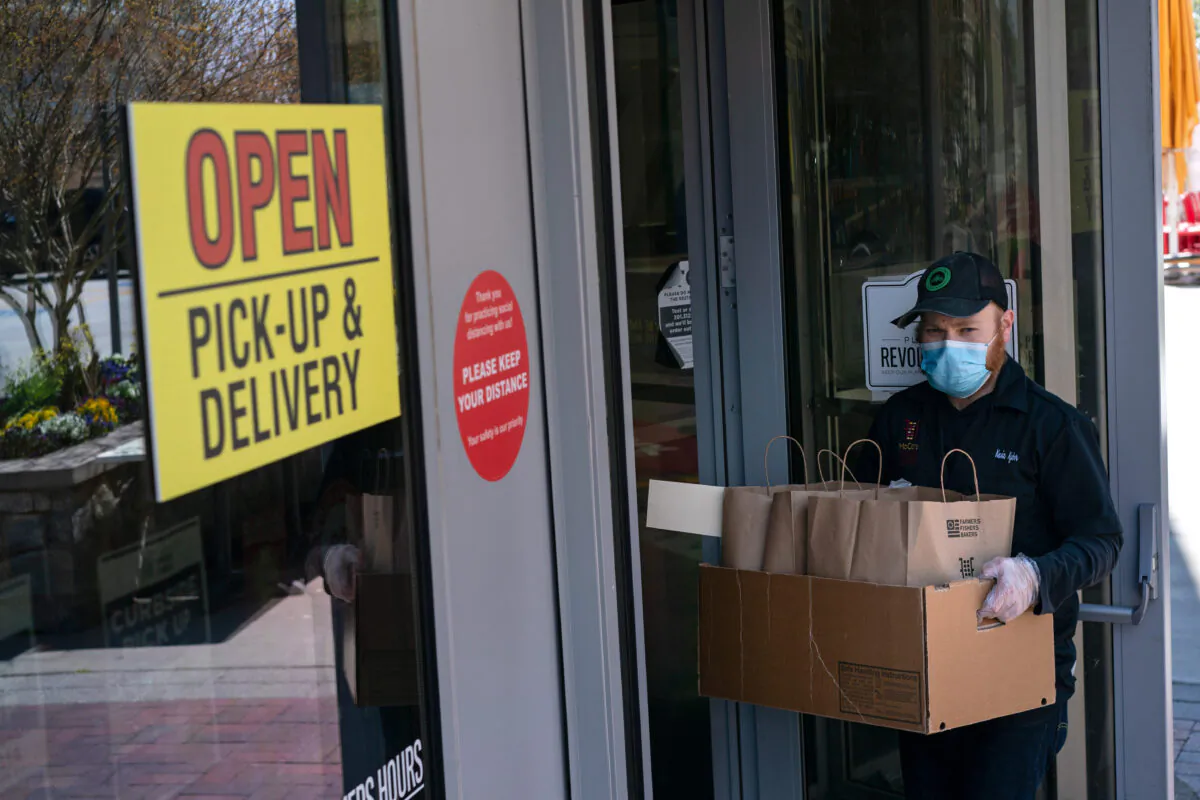 An employee wearing a mask and gloves brings to-go orders to waiting cars at a Founding Farmers restaurant in Potomac, Md., on April 15, 2020. (AP Photo/Carolyn Kaster)