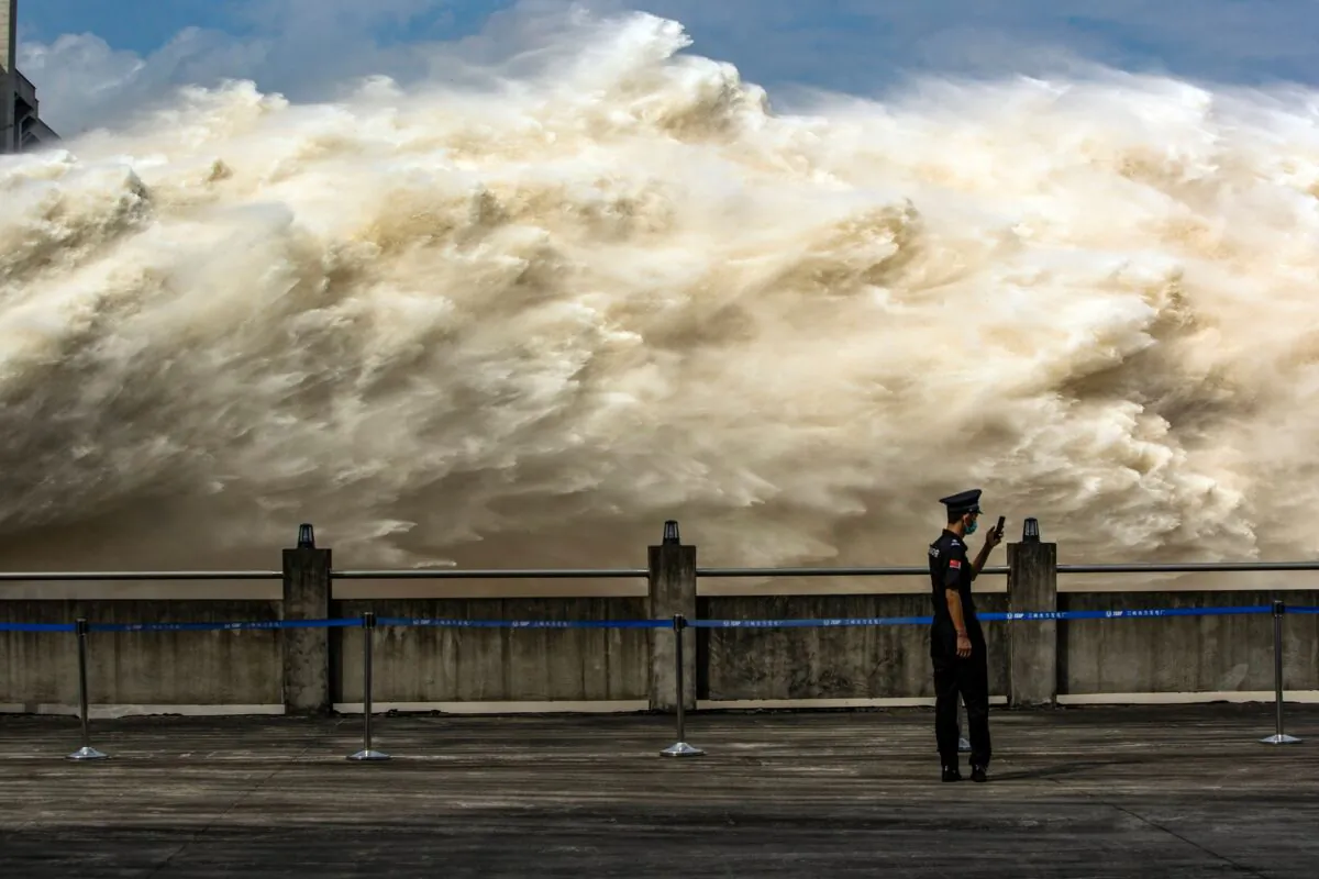 A security guard looks at his smartphone while water is released from the Three Gorges Dam, a gigantic hydropower project on the Yangtze river, to relieve flood pressure in Yichang, Hubei Province, China, on July 19, 2020. (STR/AFP via Getty Images)