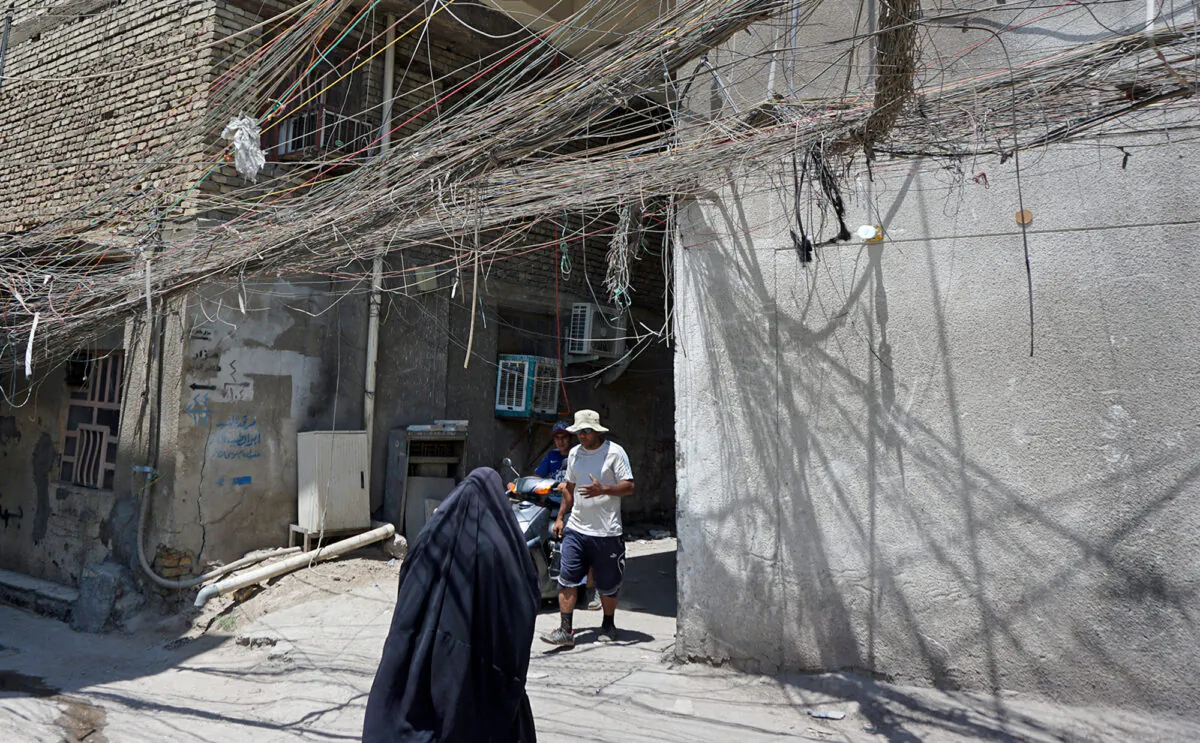 Iraqis walk beneath a web of electric wires in the Syed Sultan Ali area of the capital Baghdad, on July 13, 2020, used to draw electricity from private generators due to an unreliable national electricity supply amid high temperatures. (SABAH ARAR/AFP via Getty Images)
