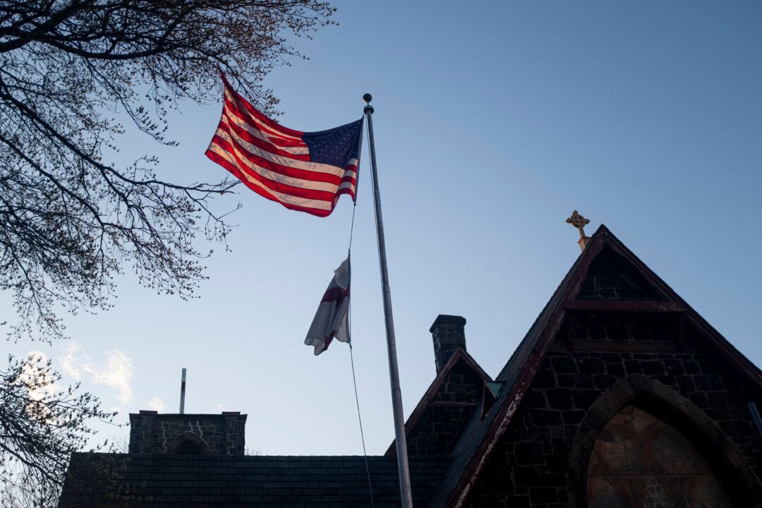 A U.S. flag is lit by the setting sun in front of the Church of the Redeemer next to the Mount Sinai Hospital in Queens, New York City, on April 15, 2020. The CCP virus pandemic is likely to have a "profound and pervasive impact" on global mental health as billions struggle to cope with isolated living and anxiety spikes, experts warned. (Johannes Eisele/AFP/AFP via Getty Images)