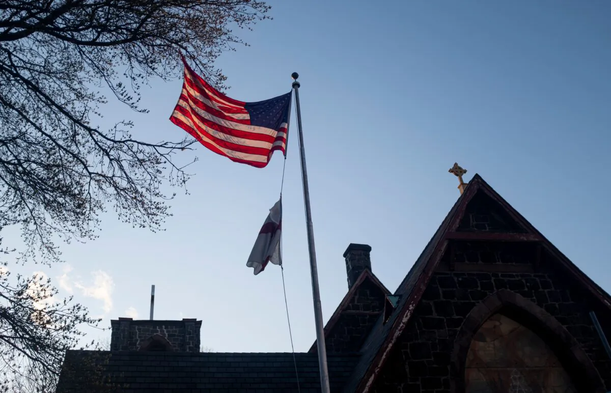 A U.S. flag is lit by the setting sun in front of the Church of the Redeemer next to the Mount Sinai Hospital in Queens, New York City, on April 15, 2020. The CCP virus pandemic is likely to have a "profound and pervasive impact" on global mental health as billions struggle to cope with isolated living and anxiety spikes, experts warned. (Johannes Eisele/AFP/AFP via Getty Images)