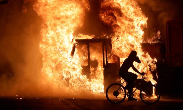 A man on a bike rides past a city truck on fire outside the Kenosha County Courthouse during riots following the police shooting of Jacob Blake in Kenosha, Wis., on Aug. 23, 2020. (Mike De Sisti/Milwaukee Journal Sentinel via USA TODAY via Reuters)