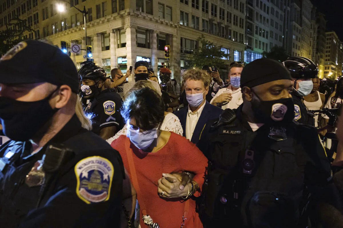 Sen. Rand Paul (R-Ky.), center, and three women are escorted by police officers through a crowd in Washington on Aug. 28, 2020. (Yuki Iwamura/AP Photo)