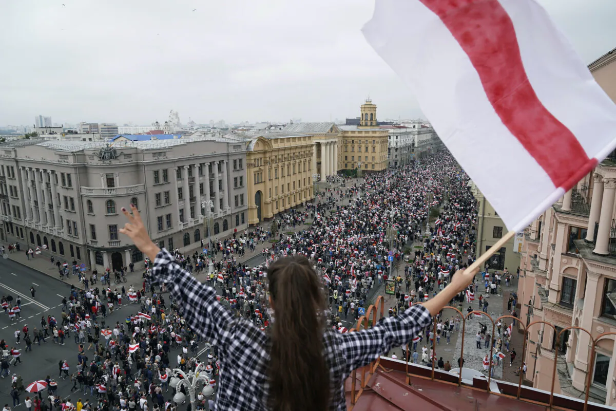 A woman waves an old Belarusian national flag standing on the roof as Belarusian opposition supporters march to Independence Square in Minsk, Belarus, on Aug. 3, 2020. (Evgeniy Maloletka/AP Photo)
