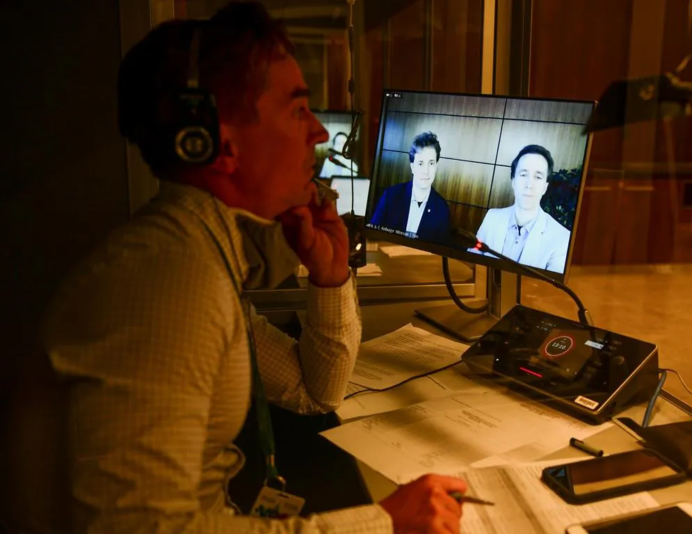 A translator works as WE Charity founders Marc Kielburger, screen (L), and Craig Kielburger, appear as witnesses via videoconference during a House of Commons finance committee in the Wellington Building in Ottawa, on July 28, 2020. (The Canadian Press/Sean Kilpatrick)