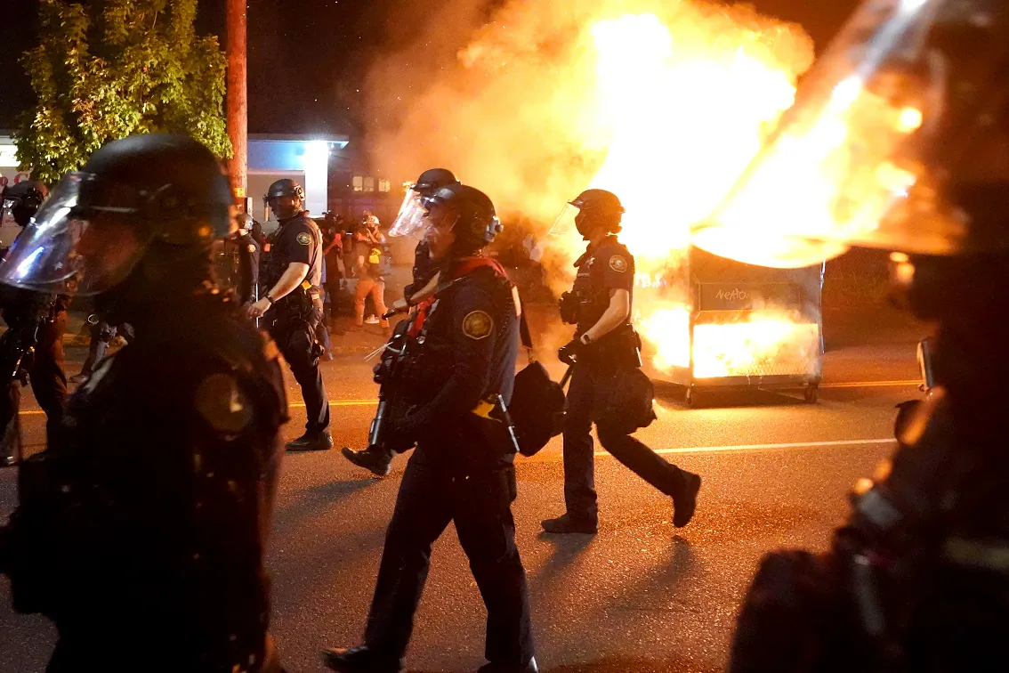 Portland police walk past a dumpster fire during a crowd dispersal in Portland, Ore., on Aug. 14, 2020. (Nathan Howard/Getty Images)