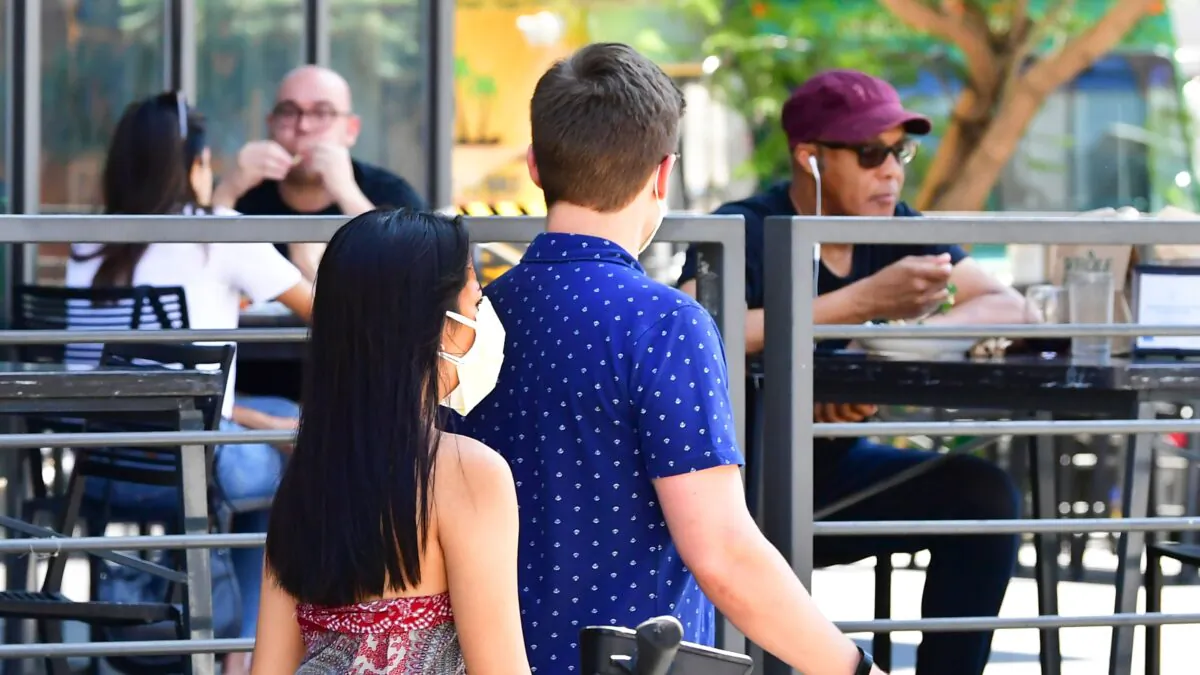 A pedestrian wears a mask while walking past people dining outdoors in Los Angeles, California, on Aug. 25, 2020. (Frederic J. Brown/AFP via Getty Images)