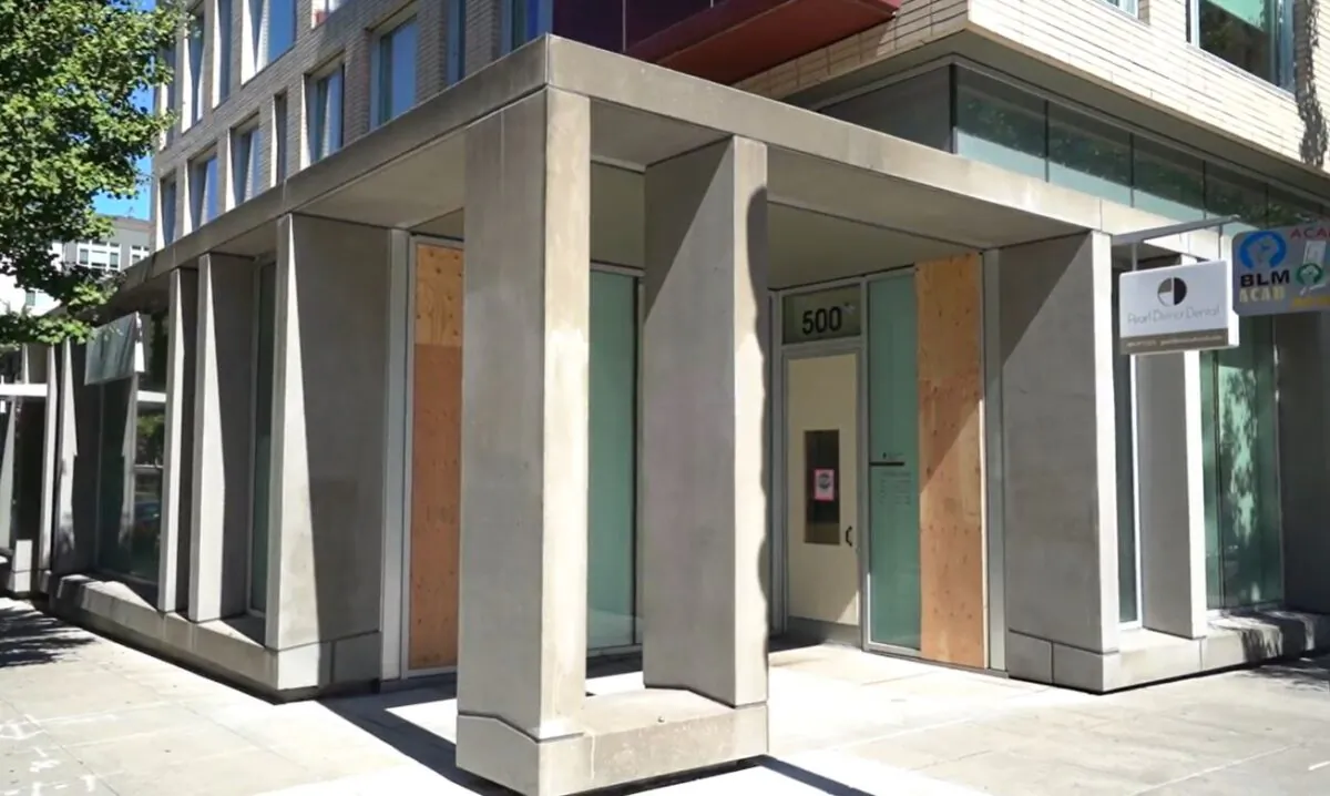 In this still image from video, boards cover glass panels destroyed recently by rioters, at Pearl District Dental, in Portland, Ore., on Sept. 2, 2020. (Roman Balmakov/The Epoch Times)