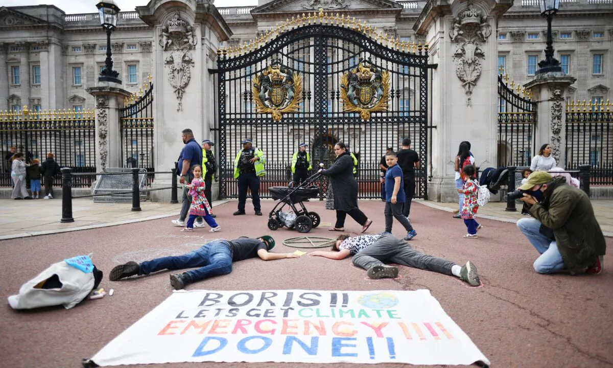 A family walk past as activists take part in a demonstration outside Buckingham Palace, as part of protests by the Extinction Rebellion climate change group on the fifth day of their new series of 'mass rebellions', in central London, on Sept. 5, 2020. (Justin Tallis/AFP via Getty Images)