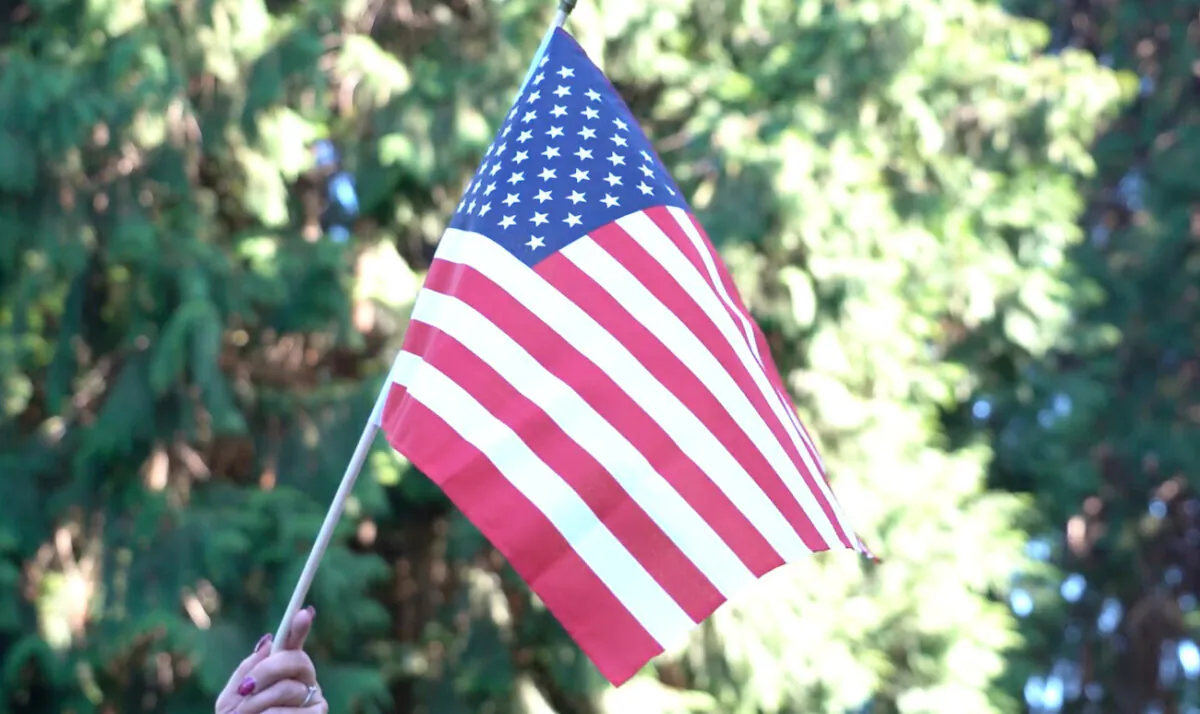 A person holds up a U.S. flag at a memorial event for Aaron “Jay” Danielson at Esther Short Park in Vancouver, Washington, on Sept. 5, 2020. (The Epoch Times)