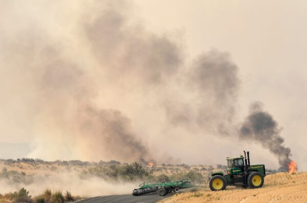 A local man runs a tractor to carve out an impromptu fire line
