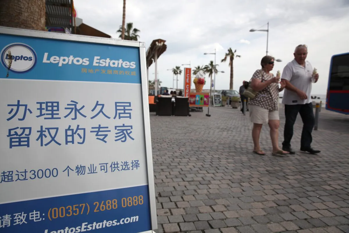 Tourists walk past a real estate promotion billboard—with text in Chinese that states buying an apartment can earn permanent resident status—on the seafront promenade in the Cypriot resort of Paphos on Jan. 24, 2013.(Yiannis Kourtoglou/AFP via Getty Images)