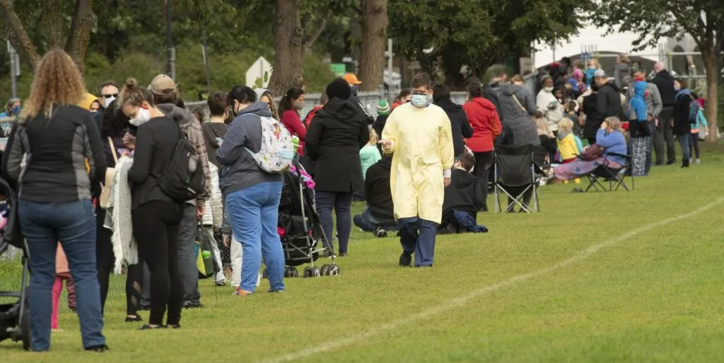 A healthcare worker walks along the line up of people waiting outside a COVID testing facility in Ottawa on Sept. 15, 2020. Several hundred people lined up on a soccer field to wait for testing. THE CANADIAN PRESS/Adrian Wyld