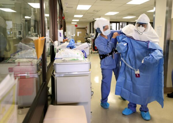 A nurse helps a doctor put on his PPE