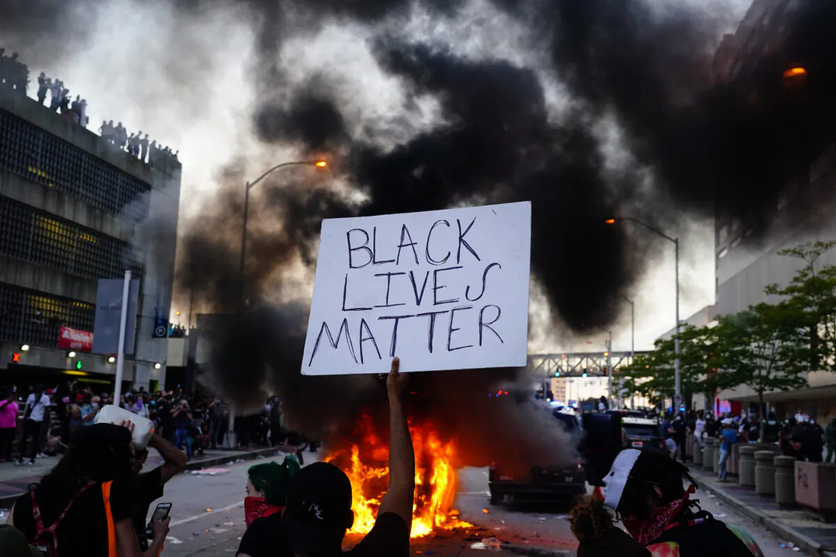 A man holds a Black Lives Matter sign as a police car burns in front of him during a protest outside CNN Center in Atlanta, Georgia on May 29, 2020. (Elijah Nouvelage/Getty Images)