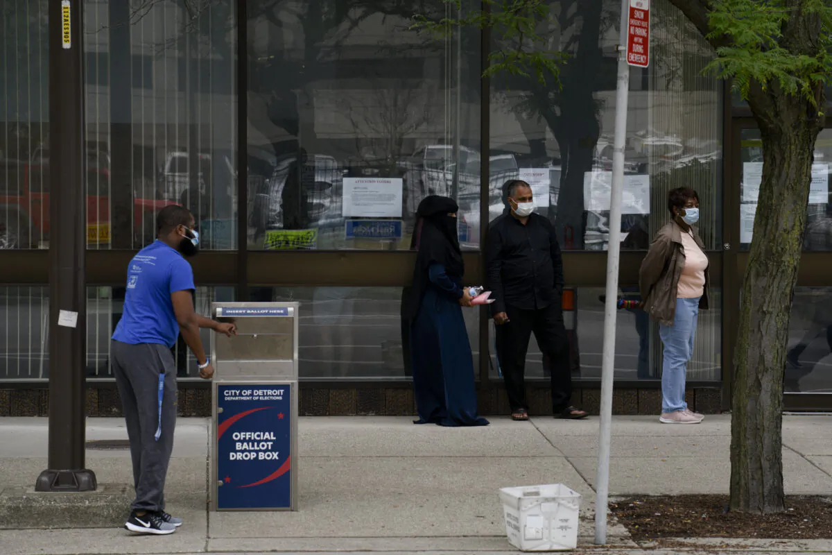 Residents keep their distance while waiting in line for same-day voter registration or amendments to their voting status as a man drops off his absentee ballot outside of the City of Detroit Department of Elections during the Michigan Primary Election in Detroit, Mich., Aug. 4, 2020. (Brittany Greeson/Getty Images)