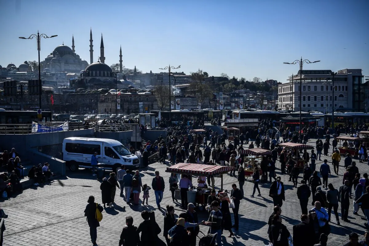 People walk in the district of Eminonu, next to bread and fish street vendors, as the Suleymaniye Mosque is seen in the background during a sunny day in Istanbul, Turkey, on April 3, 2018. (Ozan Kose/AFP via Getty Images)