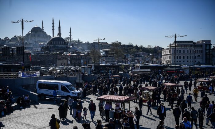 People walk in the district of Eminonu, next to bread and fish street vendors, as the Suleymaniye Mosque is seen in the background during a sunny day in Istanbul, Turkey, on April 3, 2018. (Ozan Kose/AFP via Getty Images)