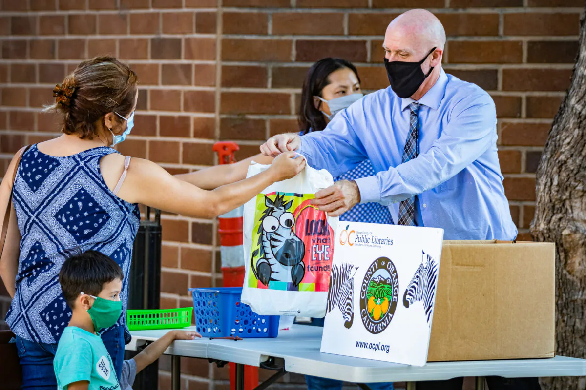 Librarian Tim Scott hands a family free children’s books at the Westminster Library in Westminster, Calif., on Sept. 22, 2020. (John Fredricks/The Epoch Times)