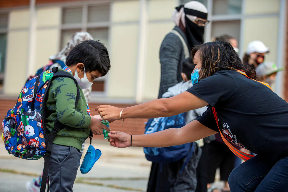 A teacher helps a student close his personal hand sanitizer as he arrives for the first time since the start of the coronavirus disease (COVID-19) pandemic at Hunter's Glen Junior Public School, part of the Toronto District School Board (TDSB) in Scarborough, Ontario, Canada September 15, 2020. (Reuters/Carlos Osorio/File Photo)
