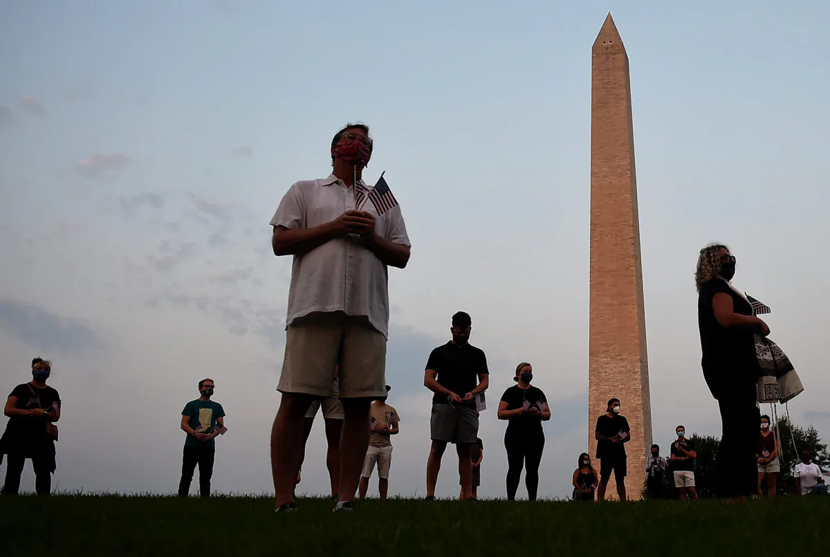 Members of the Covid Memorial Project hold American flags in front of the Washington Monument to commemorate COVID-19 victims, in Washington on Aug. 27, 2020. (Olivier Douliery/AFP via Getty Images)