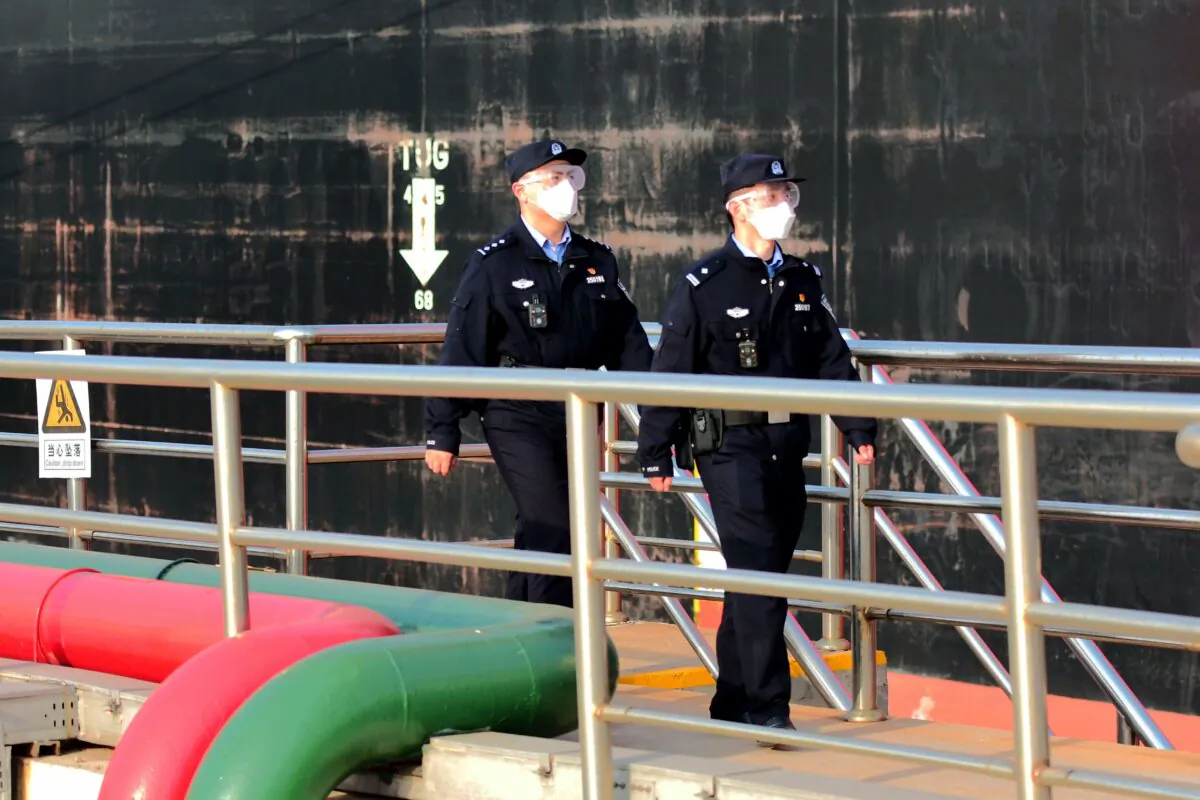 Police officers who are wearing masks watch an oil tanker unloading crude oil at the port in Qingdao, eastern China's Shandong Province on March 20, 2020. (STR/AFP via Getty Images)