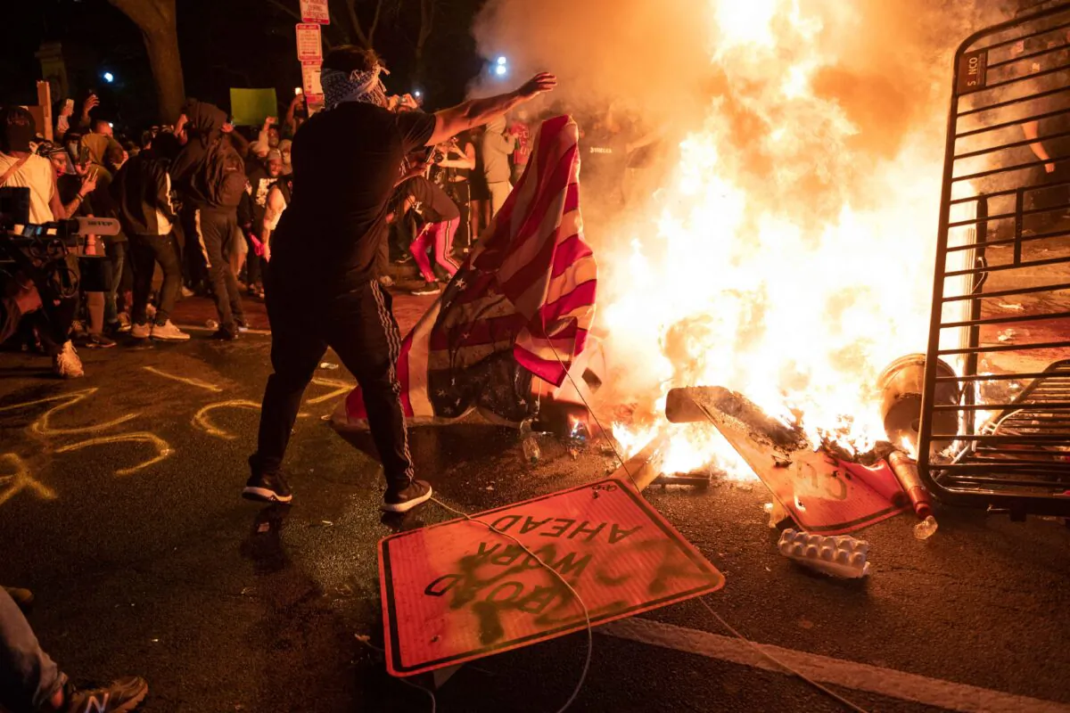 A protester throws a U.S. flag into a burning barricade during a demonstration against the death of George Floyd near the White House on May 31, 2020. (Roberto Schmidt/AFP via Getty Images)